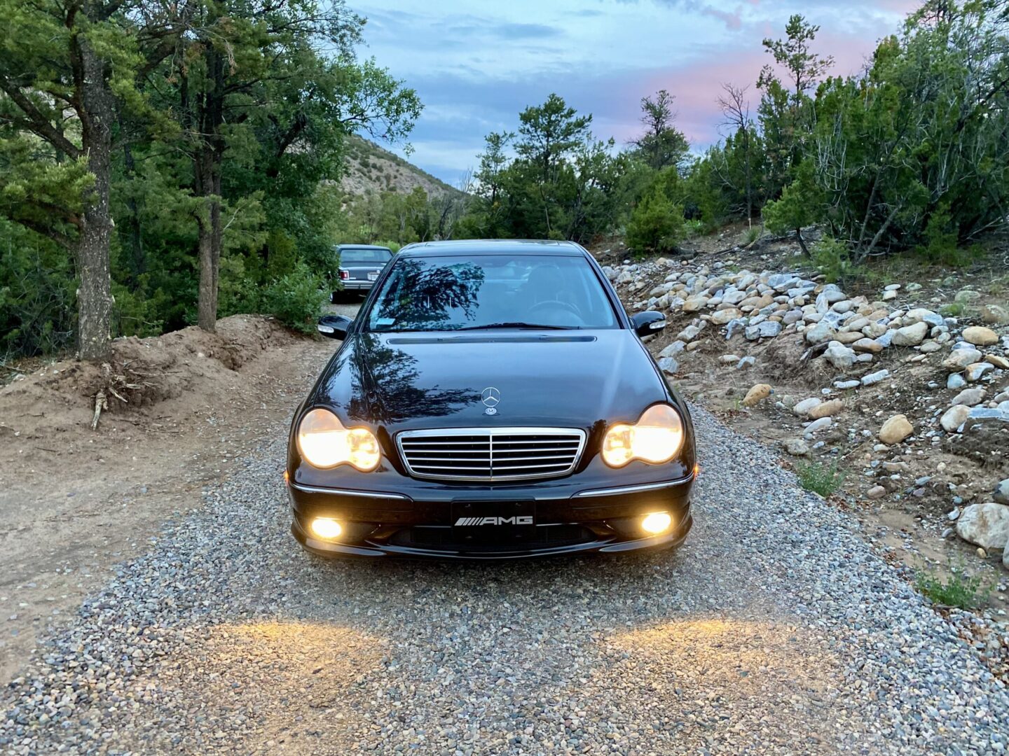 Black car on a gravel road, headlights on.